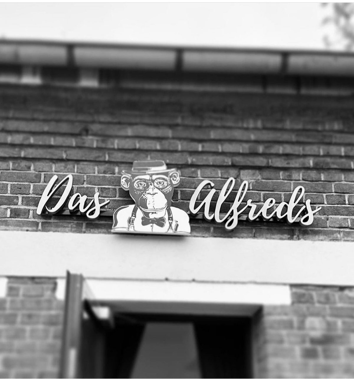 Das Leuchtschild von Das Alfreds mit Affenlogo an der Backsteinfassade
